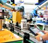 Ingenieur prüft und steuert Automatisierungsroboterarme, die eine Glaswasserflasche auf einer automatischen Industriemaschinenanlage in einer Fabrik mit Produktionslinie anordnen